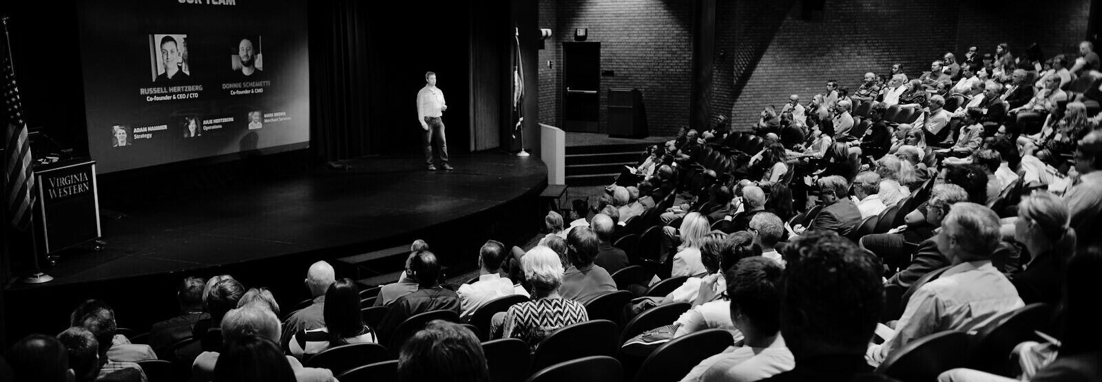 black and white photo of a man on a stage giving a presentation to an auditorium of people